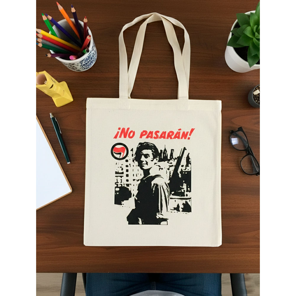 Tote bag natural ¡No Pasarán! de Ouh Rebel sobre una mesa de madera junto a una libreta y lápices de colores.