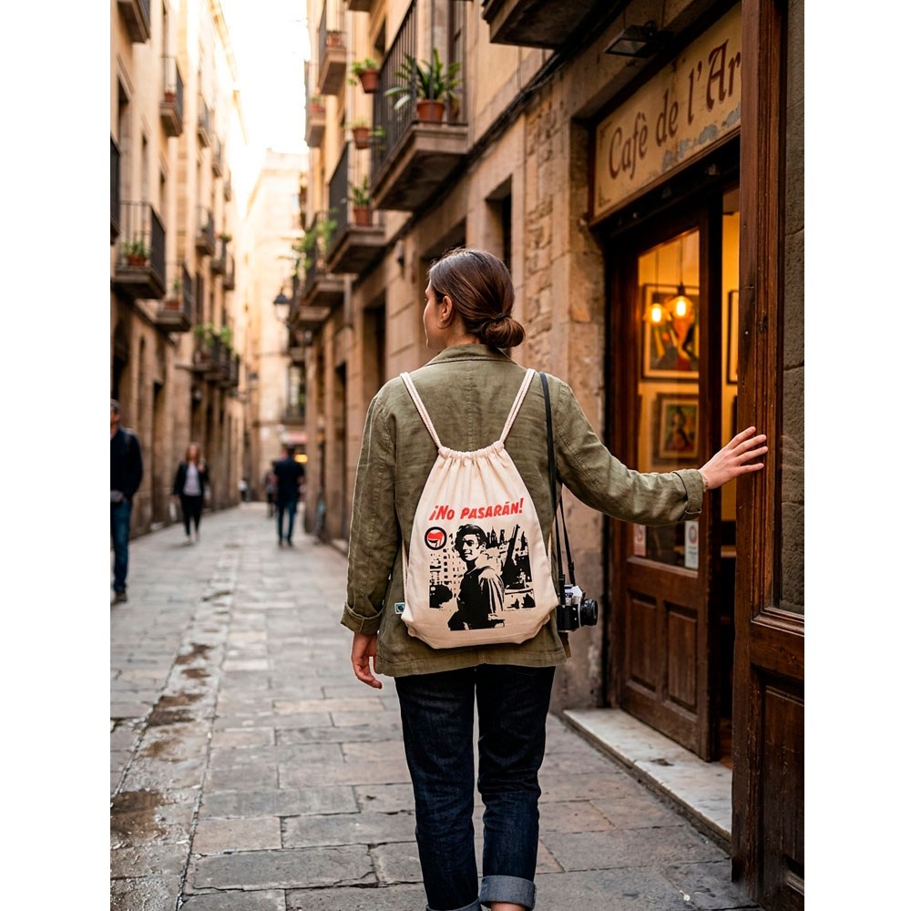 Persona de espaldas con la mochila ¡No Pasarán! de Ouh Rebel caminando por una calle peatonal estrecha de piedra.