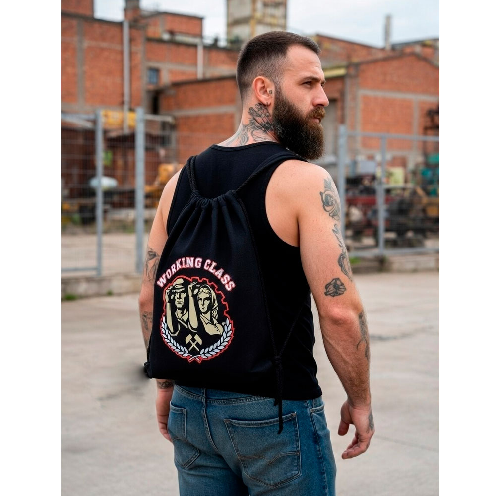 Persona de espaldas caminando con la mochila Working Class de Ouh Rebel por una zona urbana de piedra.