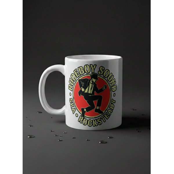 Taza blanca de Ouh Rebel con un logo circular central que muestra una ilustración de estilo cómic de un hombre bailando ska sobre un fondo rojo, con el texto "RUDEBOY SOUND · SKA · ROCKSTEADY" alrededor.