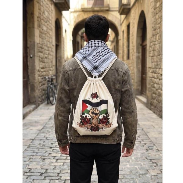 Chico de espaldas caminando por una calle empedrada con una cazadora, una kufiyya al cuello y la mochila de cuerdas Free Palestine Revolution de Ouh Rebel.